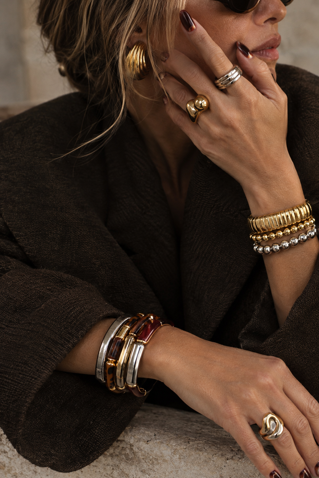 Mixed bracelet stack of gold, silver and tortoiseshell cuffs worn with a dark knit coat