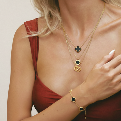 Woman wearing a gold necklace and bracelet with clover-shaped charms on a beige background